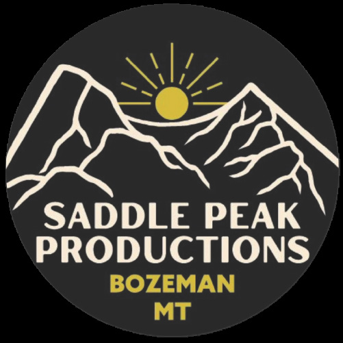 A circular logo for Saddle Peak Productions, based in Bozeman, Montana. The logo features a black background with two stylized white mountain peaks, outlined in an angular design. A golden sun with radiating lines is positioned above the peaks. Below the illustration, the text 'SADDLE PEAK PRODUCTIONS' is written in bold, uppercase, white letters, while 'BOZEMAN MT' appears in smaller, uppercase, golden-yellow letters beneath it.