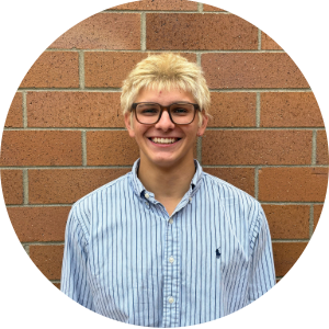 man with blonde hair and glasses in front of a brick wall