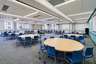 Classroom with ten group tables, an instructor podium, and projector screens