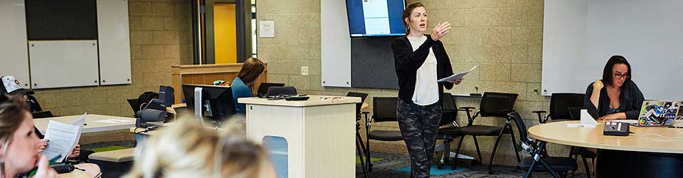 Instructor in a classroom with students at group tables